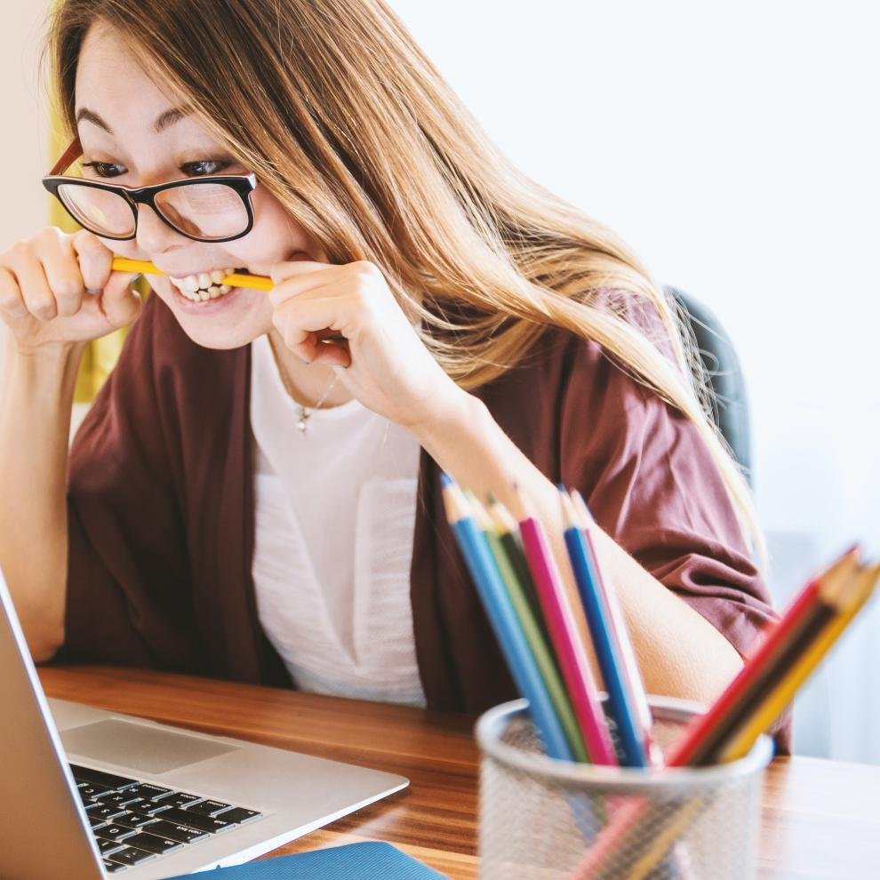 A girl bitting a pencil and looking at the computer screen